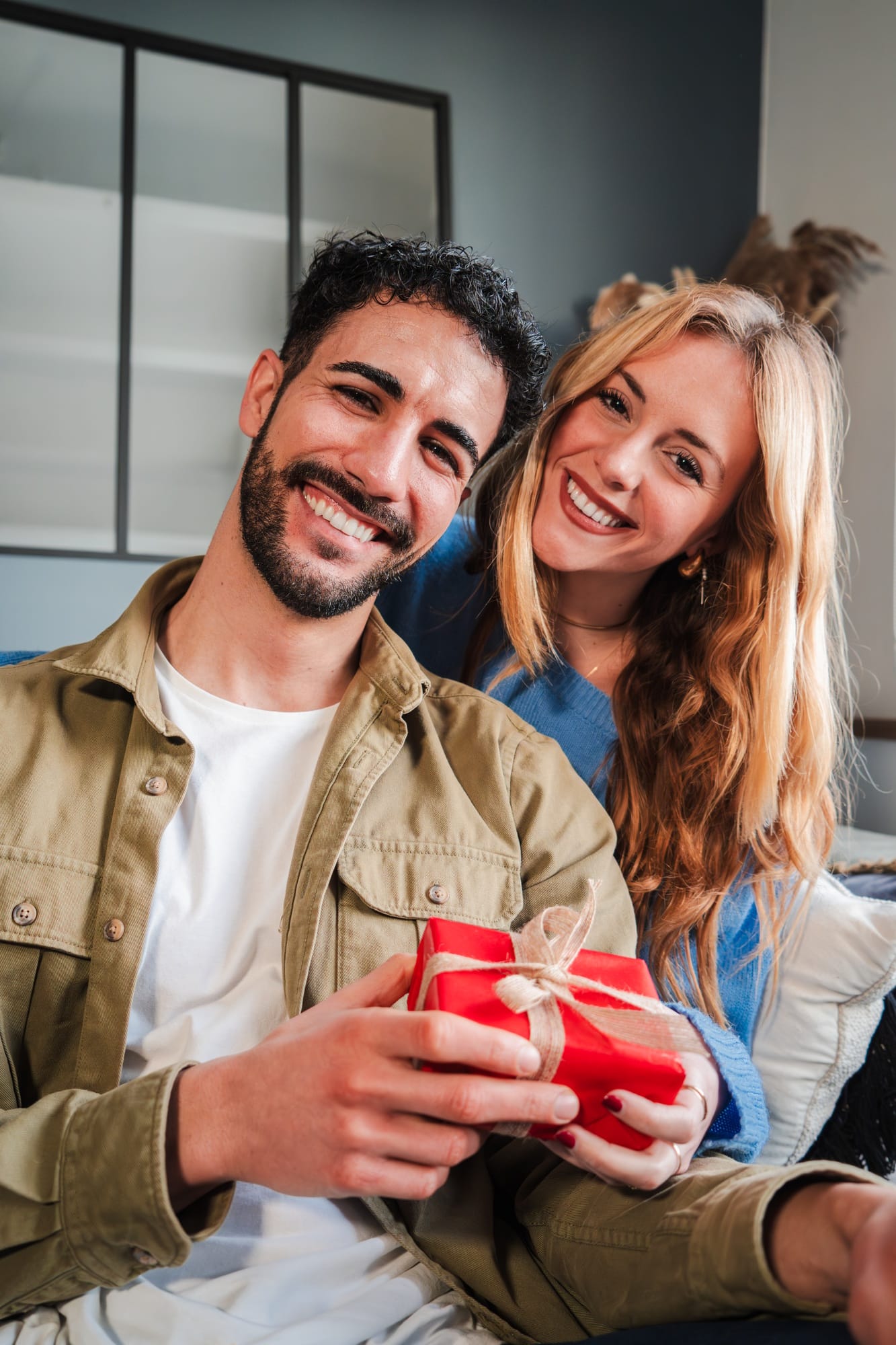Vertical. Real young couple smiling looking at camera showing a birthday gift. Man holding a